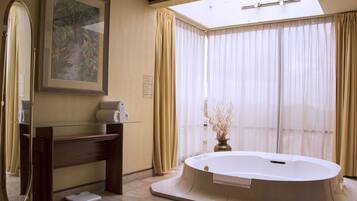 A bathroom with a glass vanity, a large mirror, a framed painting, a bathtub, and sheer curtains.