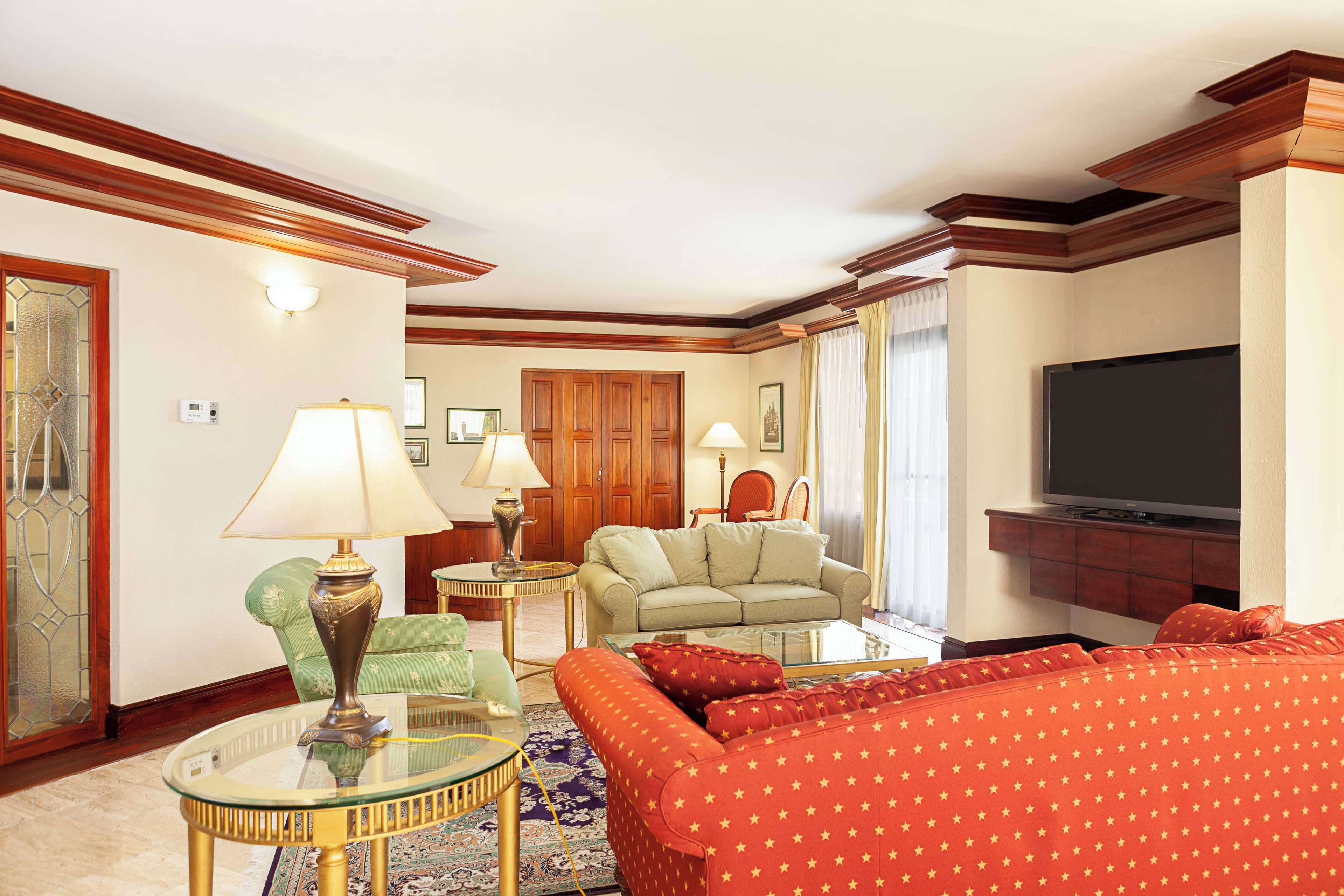 A living room with a sofa, a glass coffee table, a lamp, a television, and a wooden cabinet.