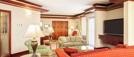 A living room with a sofa, a glass coffee table, a lamp, a television, and a wooden cabinet.