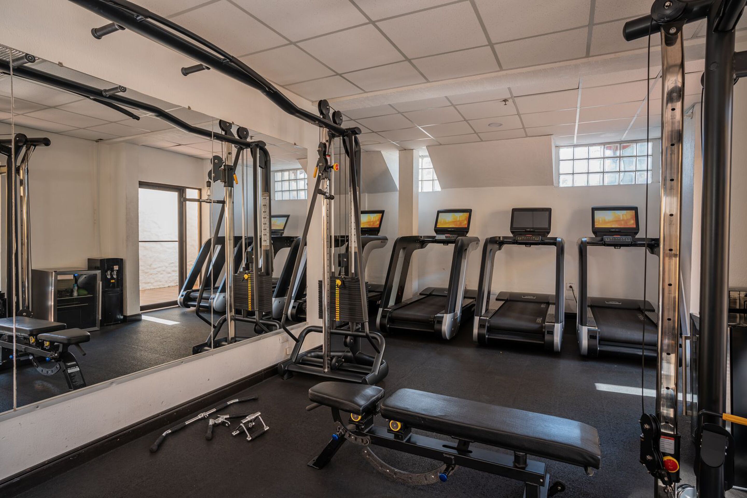A gym with exercise equipment, treadmills, and a mirrored wall.