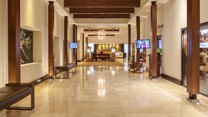 Un vestíbulo de hotel con piso de mármol pulido, vigas de madera en el techo, un mostrador de recepci ón y un área de estar con sillones.