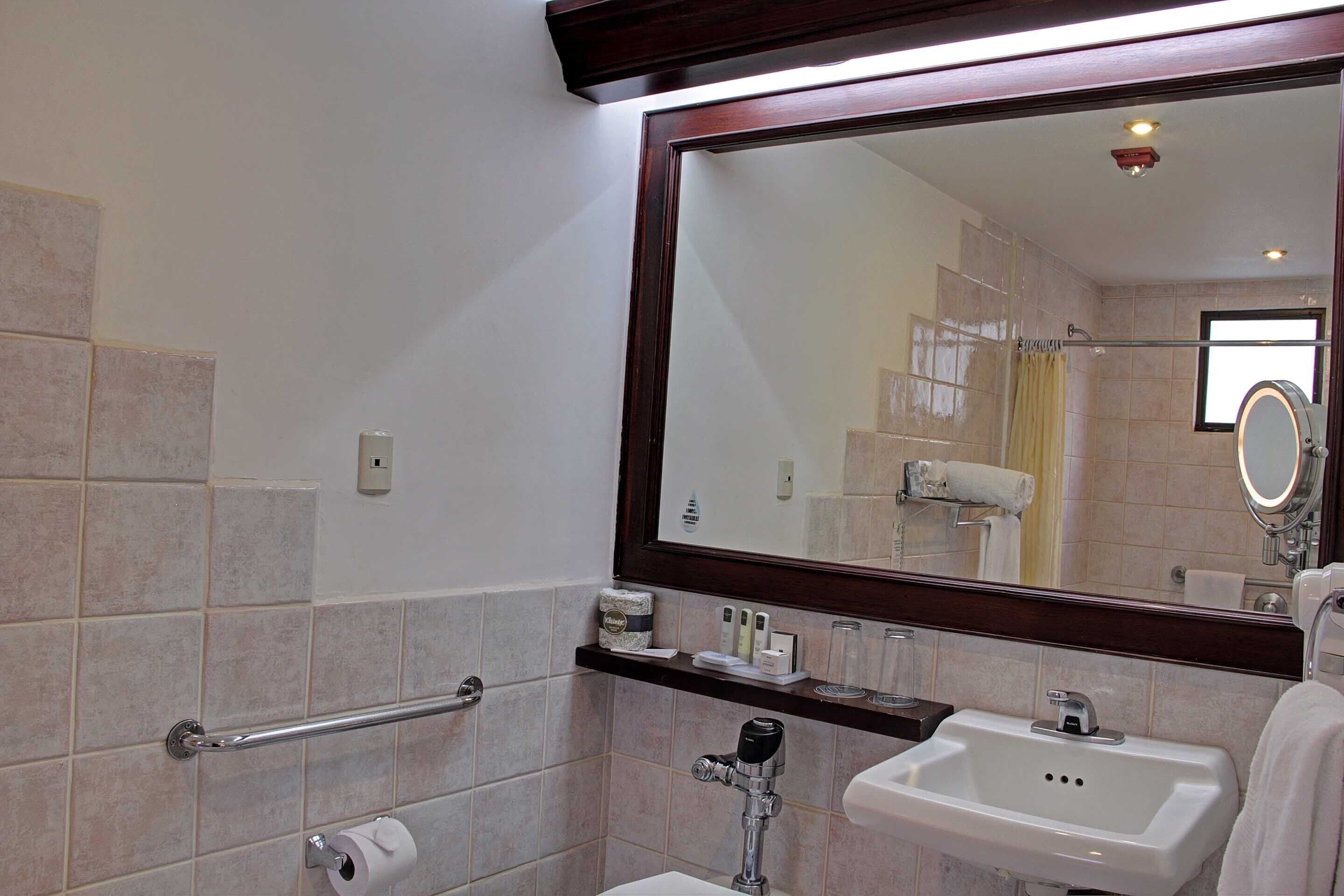 A bathroom with a large mirror, a sink, a toilet, and a shower area.