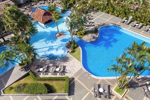 A large, clear swimming pool surrounded by lounge chairs and palm trees, with a small building in the background. - Wyndham San Jose Herradura Hotel & Convention Center (La Asunción)