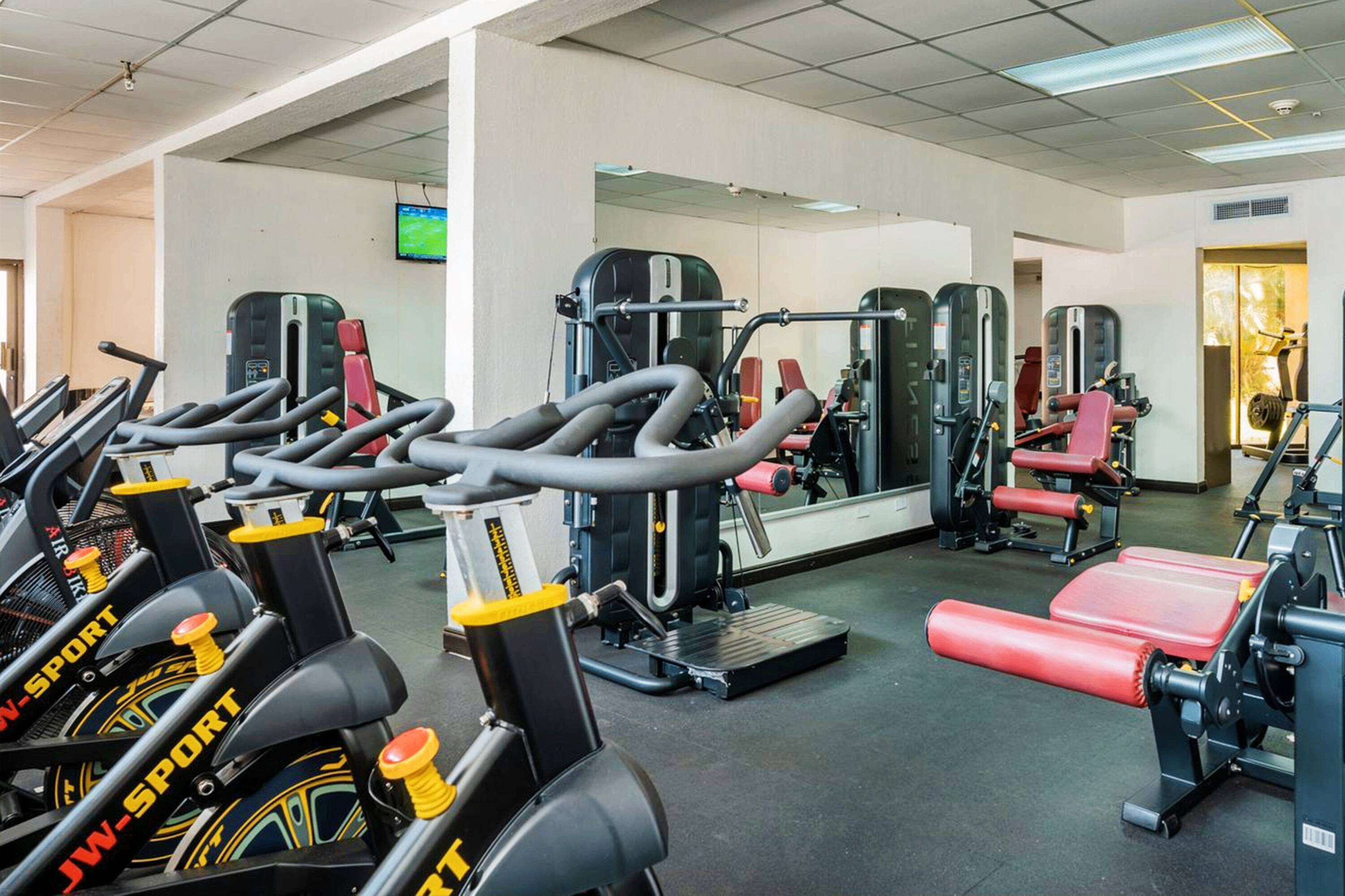 Une salle de sport équipée de divers appareils, notamment des tapis de course, des appareils de musculation et un banc rouge.