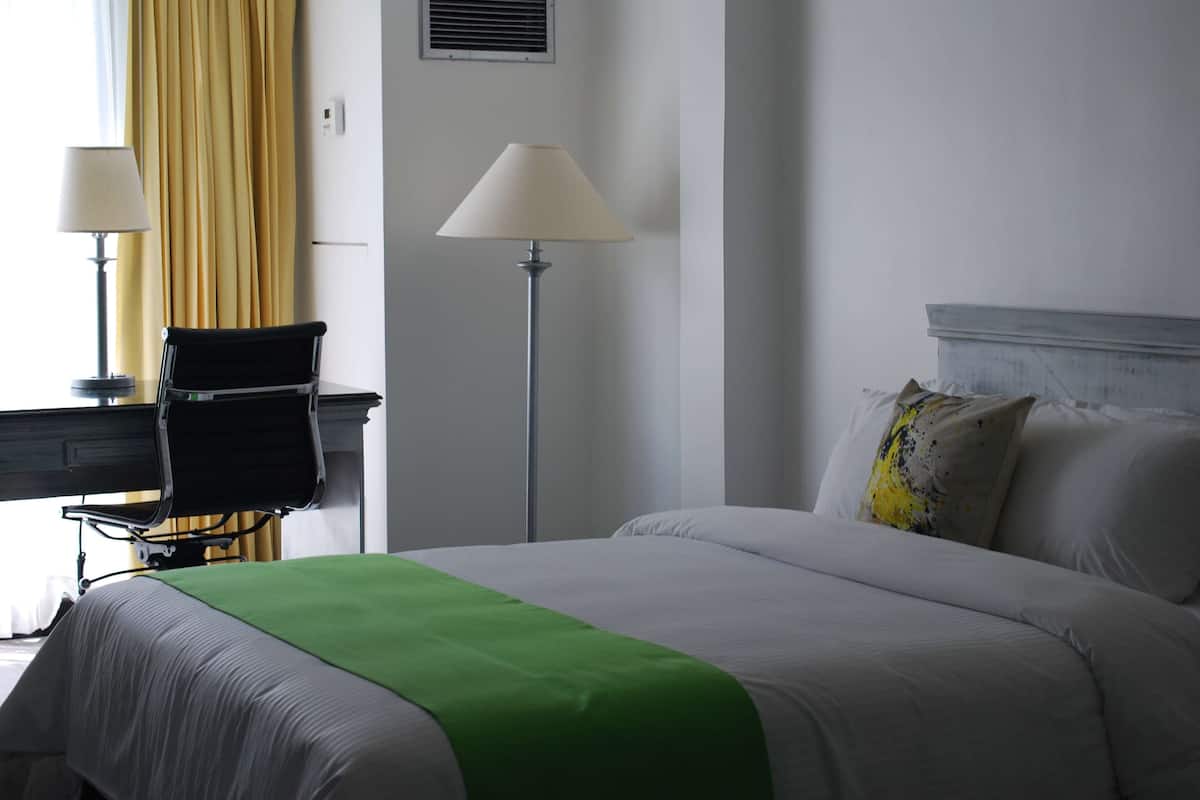 A hotel room with a bed, two lamps, a chair, and a window with curtains.