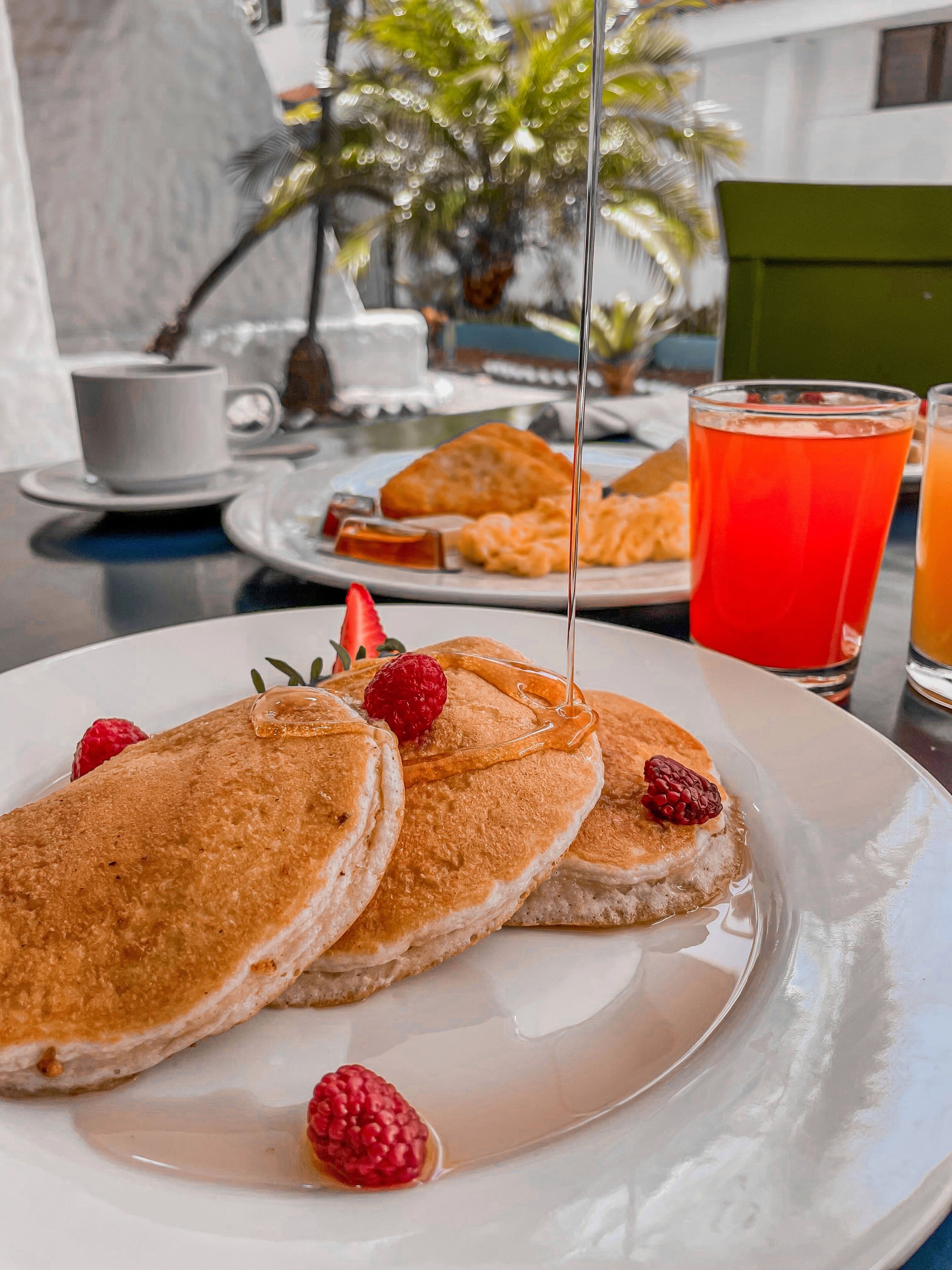 A breakfast setting with pancakes, raspberries, and syrup on a plate.
