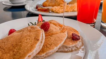 A breakfast setting with pancakes, raspberries, and syrup on a plate.