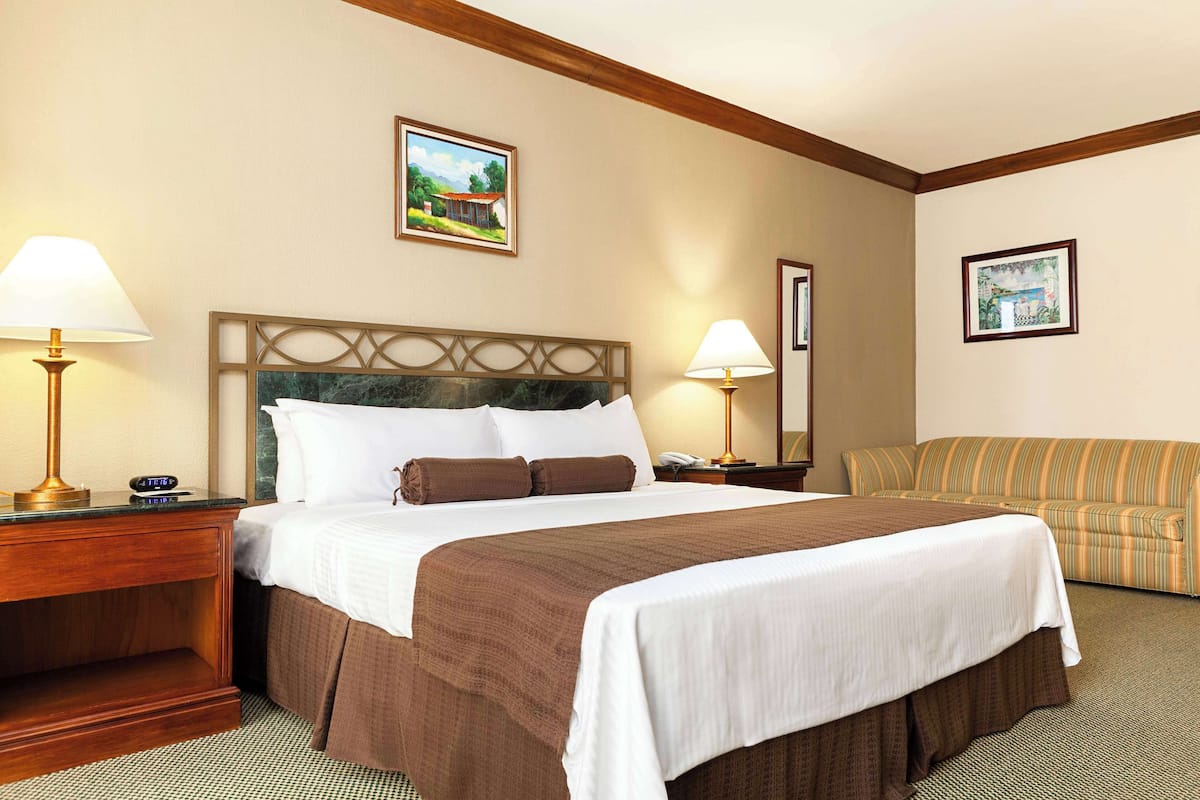 A hotel room with a large bed, two bedside tables with lamps, a sofa, and framed pictures on the walls.