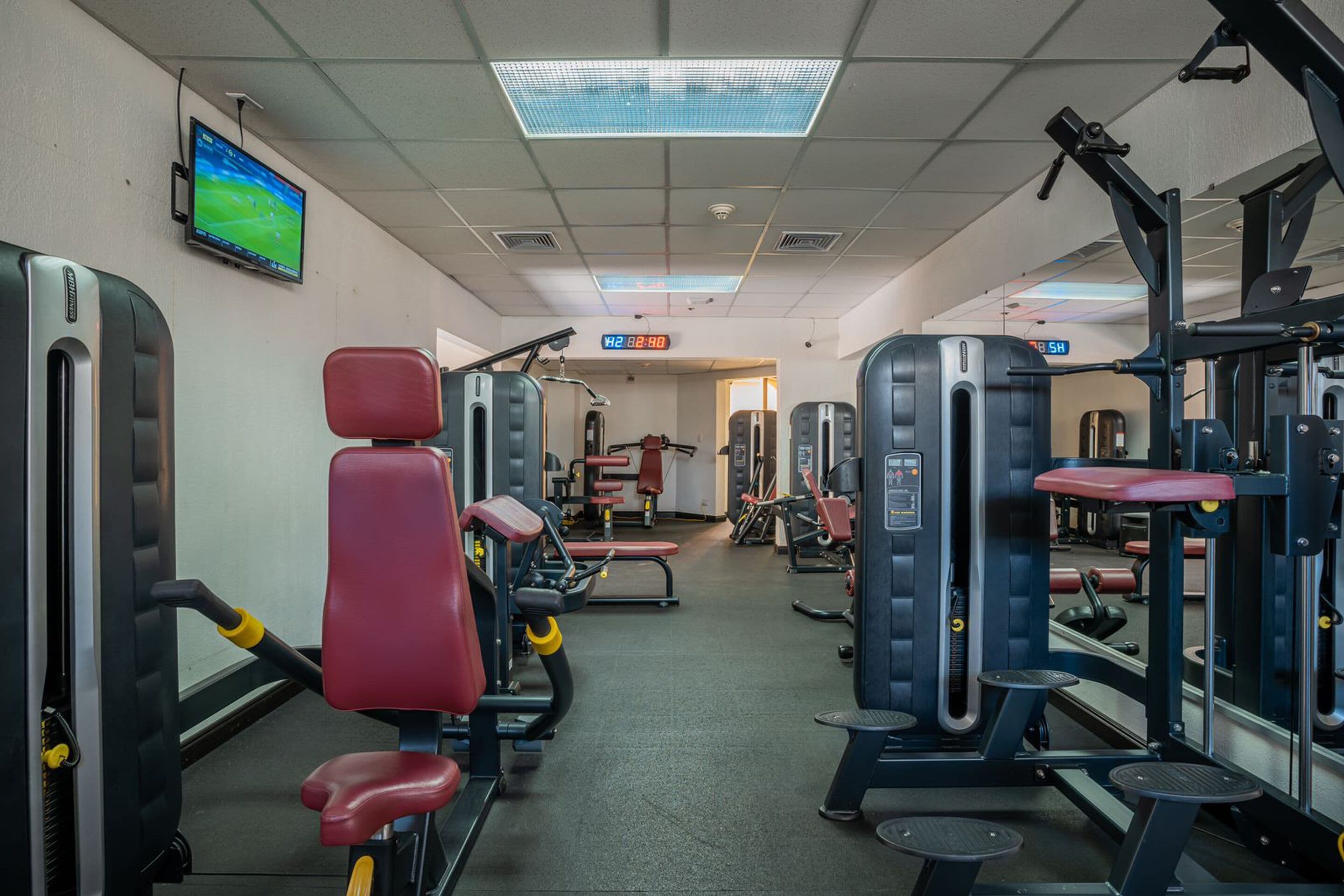 A gym with various exercise machines, a television on the wall, and a digital clock displaying the time.