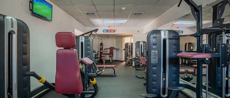 A gym with various exercise machines, a television on the wall, and a digital clock displaying the time.