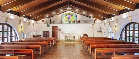A church interior with wooden pews, a stained glass window, and a tiled floor.