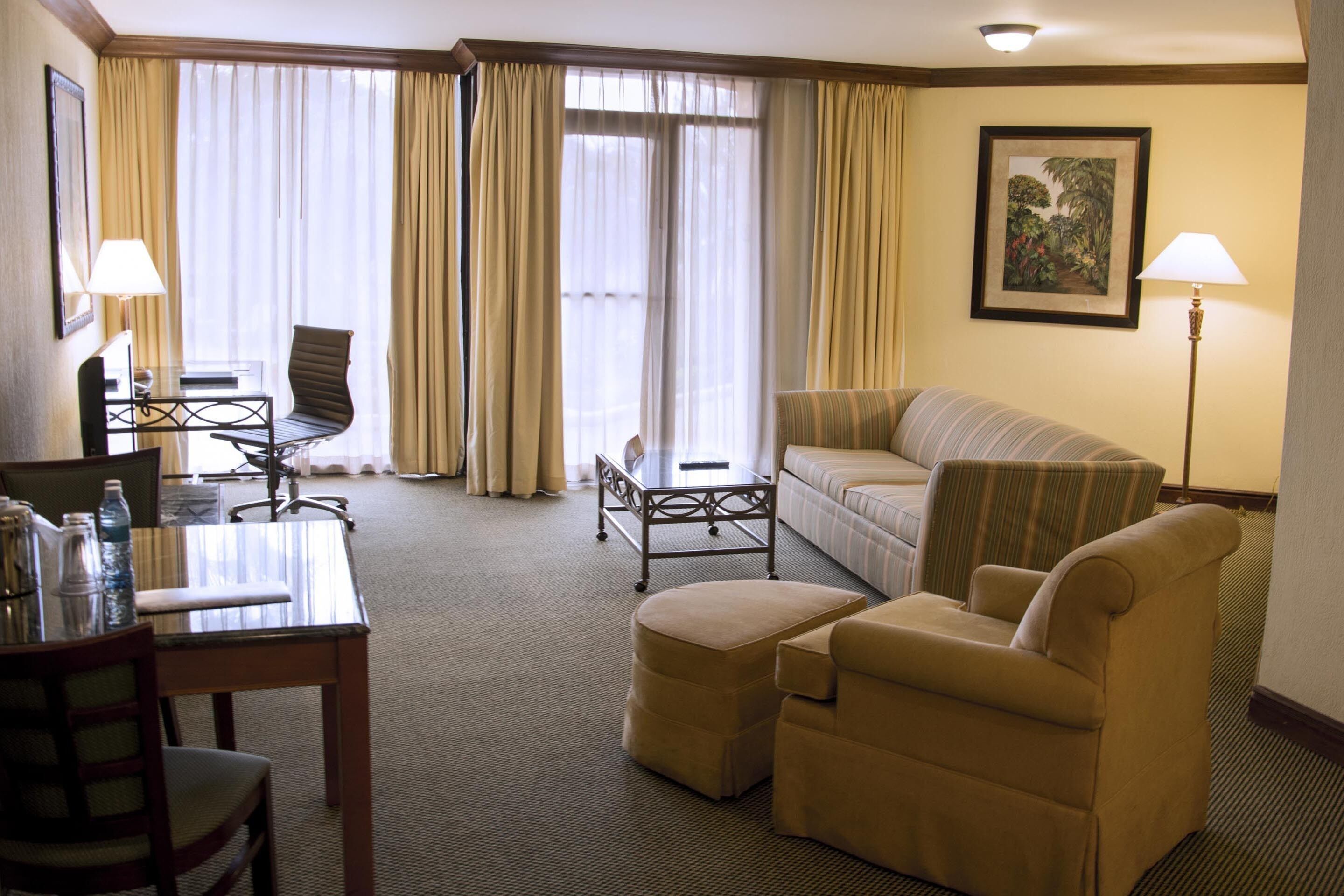 A hotel room with a sofa, armchair, dining table, and a small side table.
