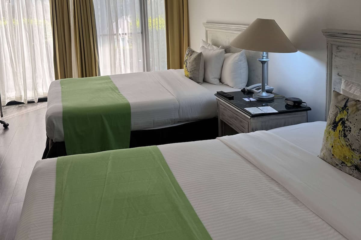 A hotel room with two beds, each with a green and white bedspread, a bedside table with a lamp, and a telephone.