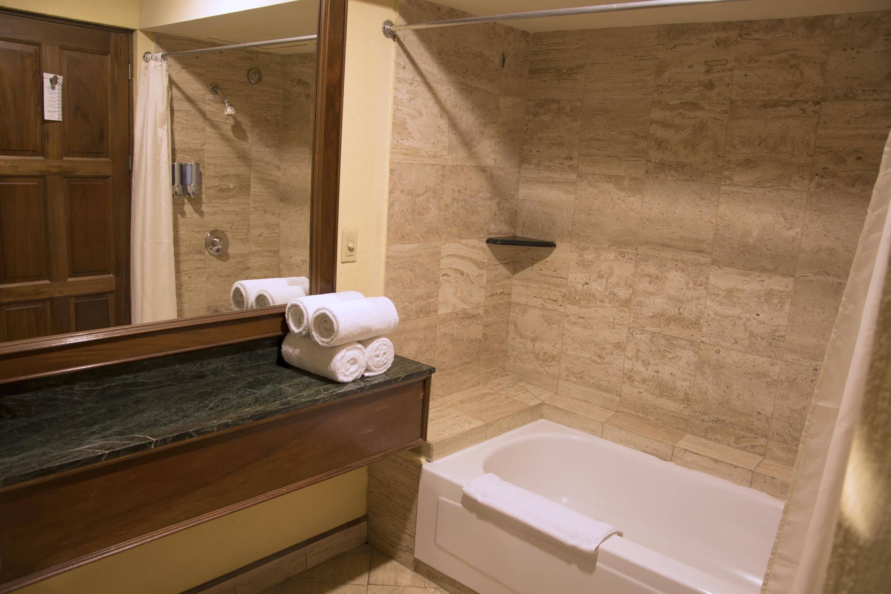 A bathroom with a bathtub, a shower, and a vanity with a mirror.