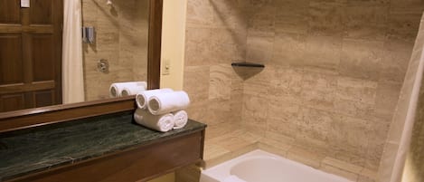 A bathroom with a bathtub, a shower, and a vanity with a mirror.