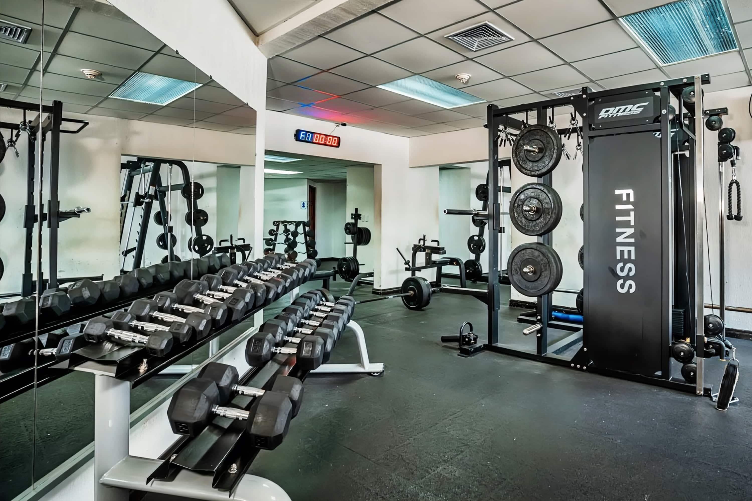 A gym with weightlifting equipment, a digital clock, and a mirrored wall.