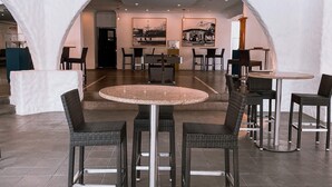 Un moderno comedor interior con mesas redondas y sillas de mimbre, que cuenta con una isla central y fotografías blanco y negro enmarcadas en las paredes.