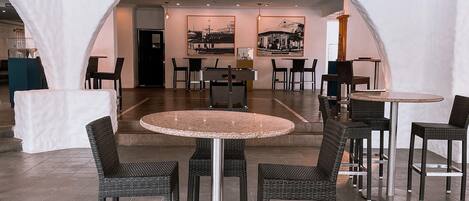 A modern indoor dining area with round tables and wicker chairs, featuring a central island and framed black-and-white photographs on the walls.