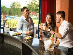 Un espace bar avec vue sur la piscine, des places assises en plein air et un aménagement propice à une restauration décontractée.