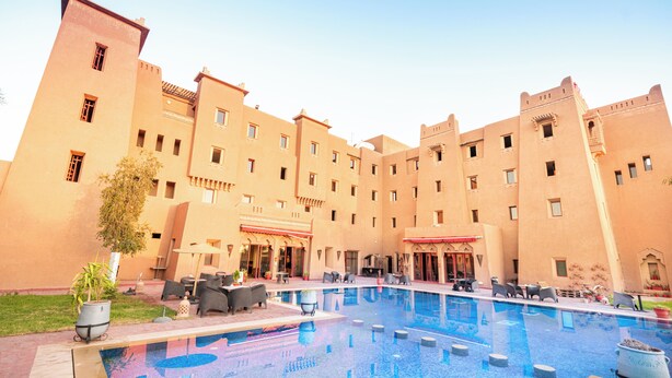 Une cour d’hôtel avec une piscine, des espaces de détente en plein air et un grand bâtiment doté de nombreuses fenêtres et de balcons.