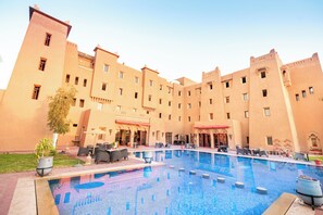 Une cour d’hôtel avec une piscine, des espaces de détente en plein air et un grand bâtiment doté de nombreuses fenêtres et de balcons.