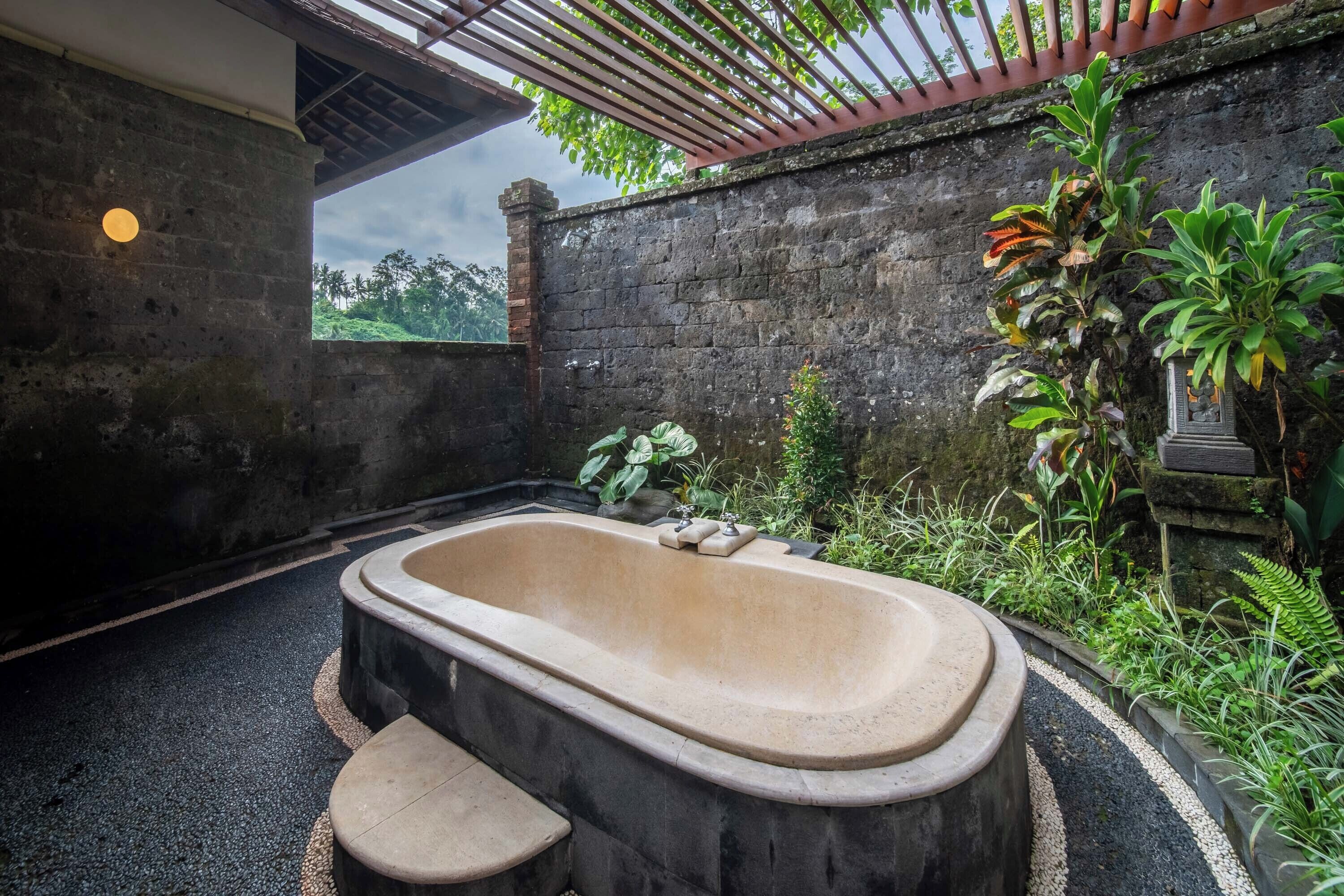 A spa area with a large bathtub, steps leading into it, and lush greenery around.