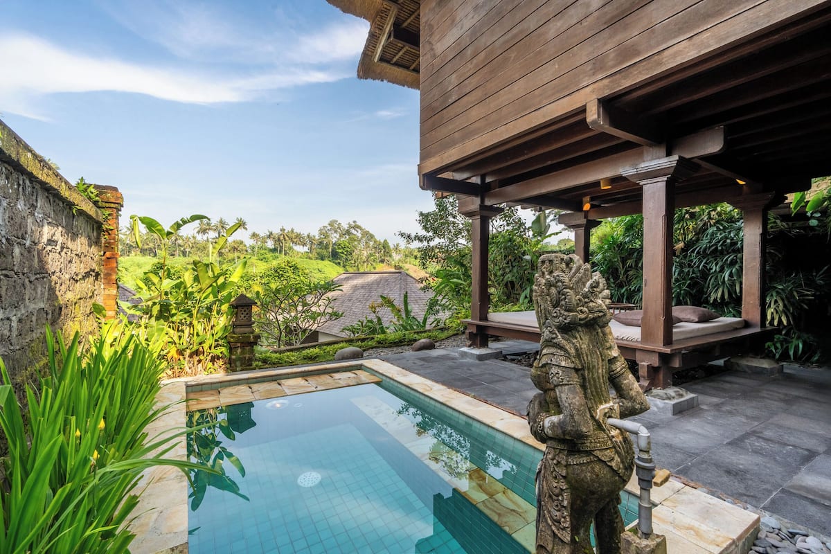 Une piscine ornée d’une statue en pierre, un pergolas en bois et une végétation luxuriante.