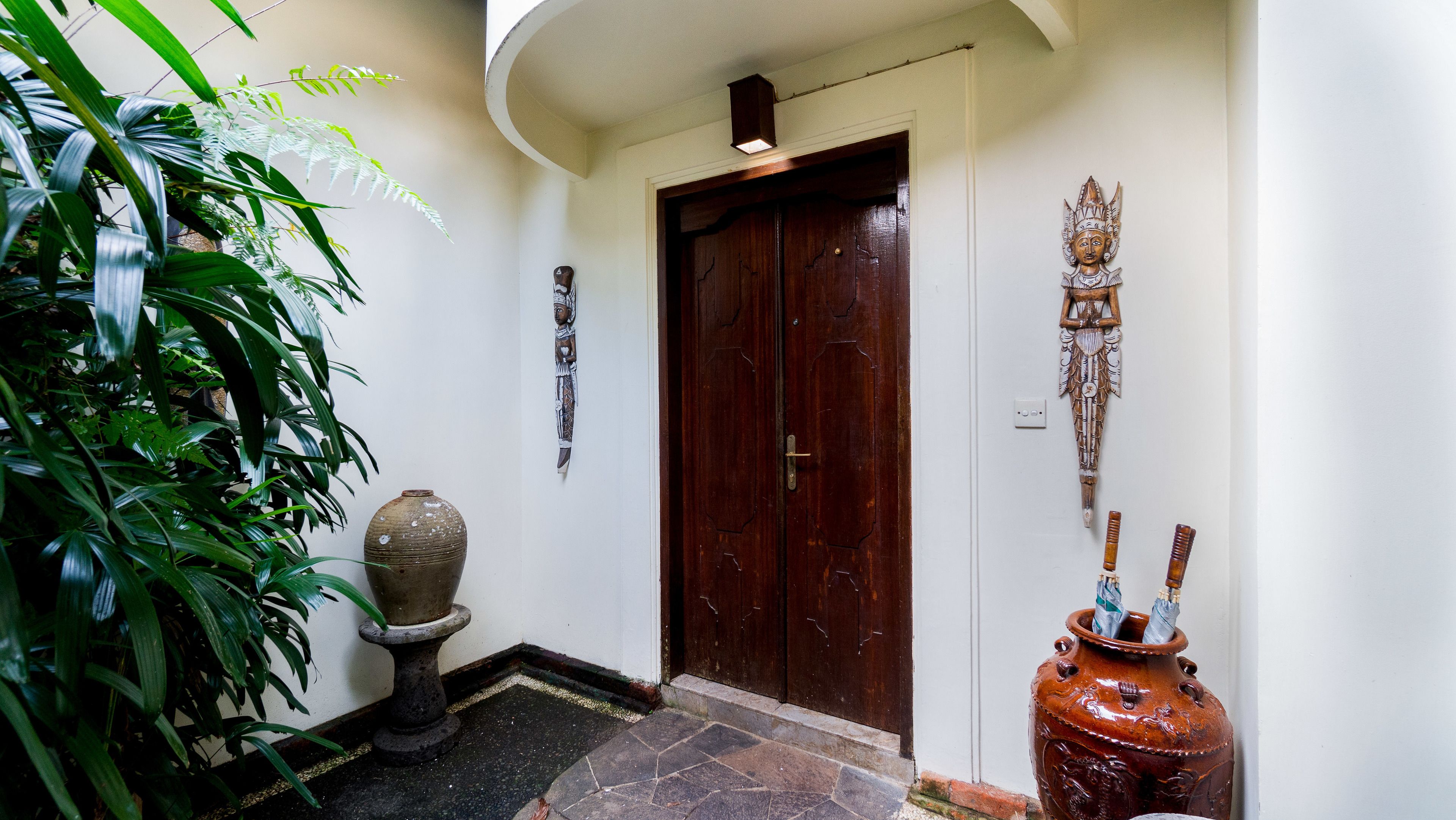 A hallway with a wooden door, a large vase, and a decorative mask on the wall.