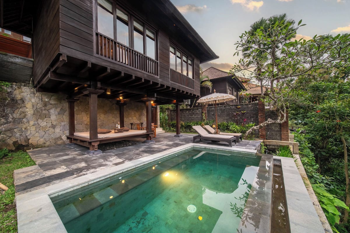 Un espace aménagé au bord de la piscine, avec un mur en pierre, une terrasse en bois et un bâtiment à deux étages doté d’un balcon.