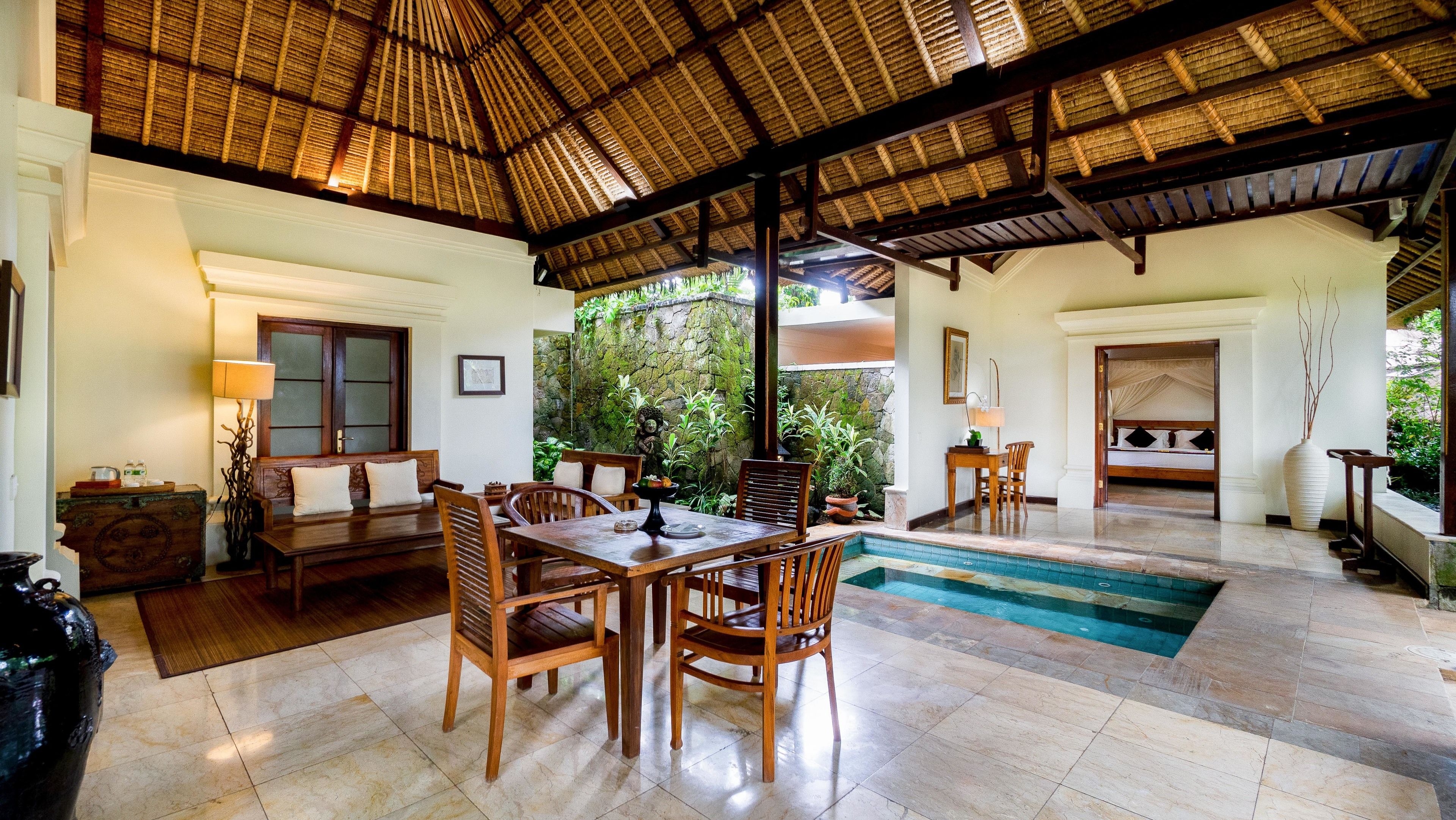 Une pièce spacieuse avec un toit de chaume, un coin repas avec des meubles en bois, une petite piscine et une chambre séparée comprenant un lit et un grand vase.