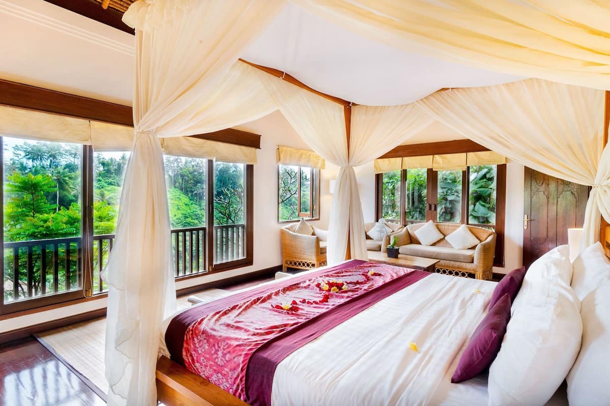 Une chambre à coucher avec un lit à baldaquin, un canapé et de grandes fenêtres donnant sur un paysage verdoyant.