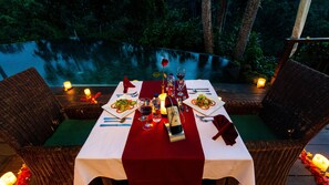 An outdoor dining setup with a table set for two, surrounded by wicker chairs, and candles on the table.