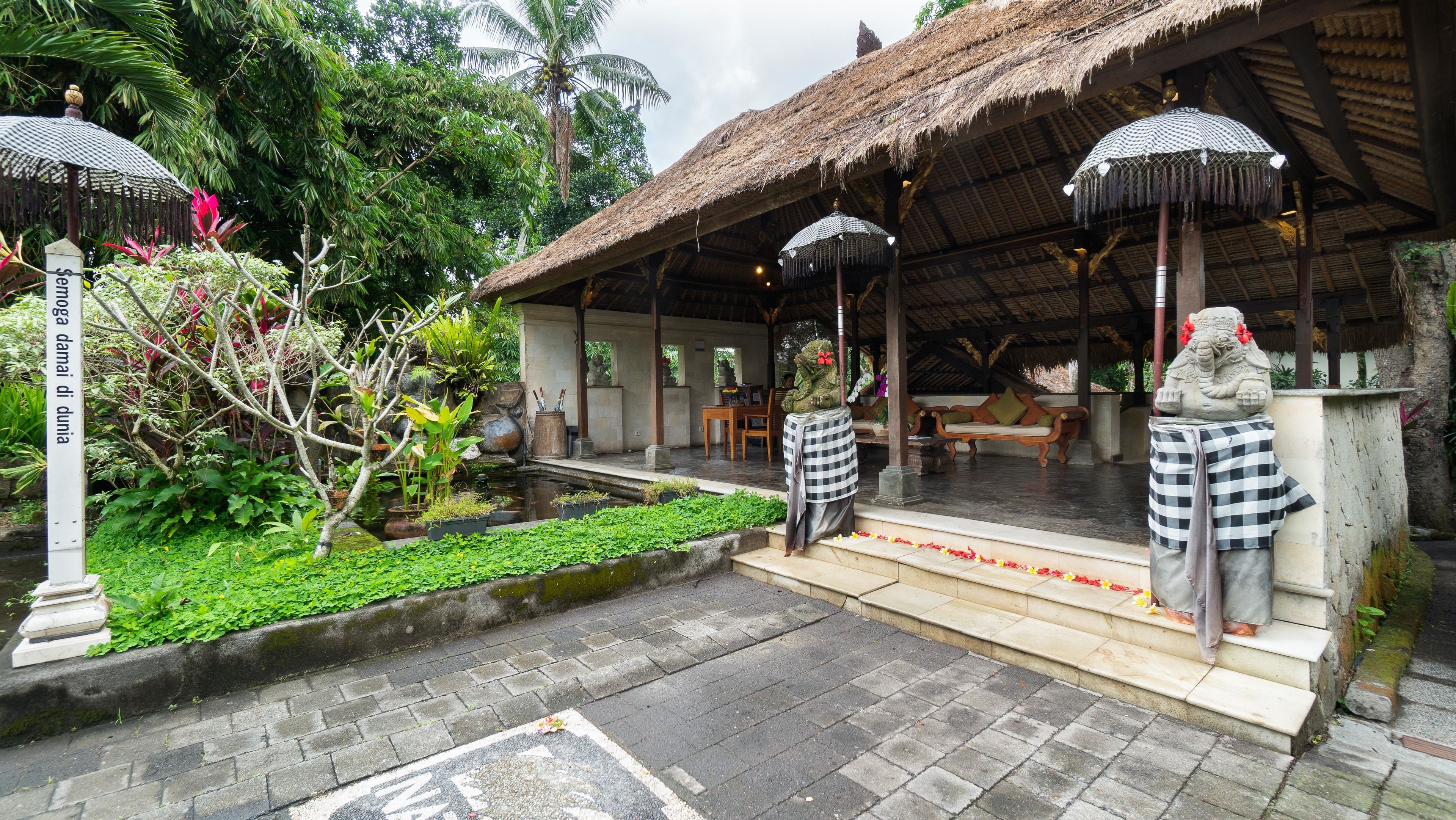A traditional Balinese structure with a thatched roof, a stone statue, and a small pond.