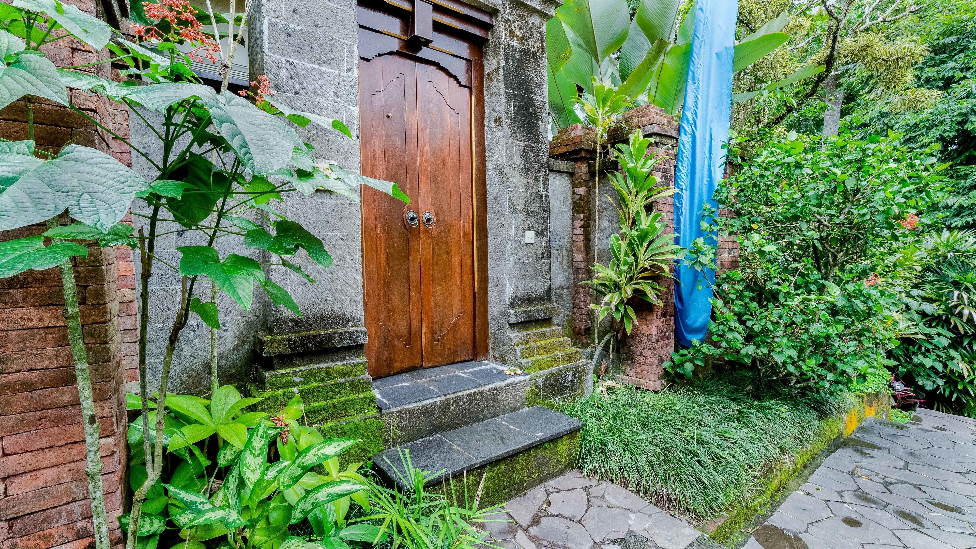 A traditional wooden door with a stone wall, a brick staircase, and lush greenery surrounding the entrance.