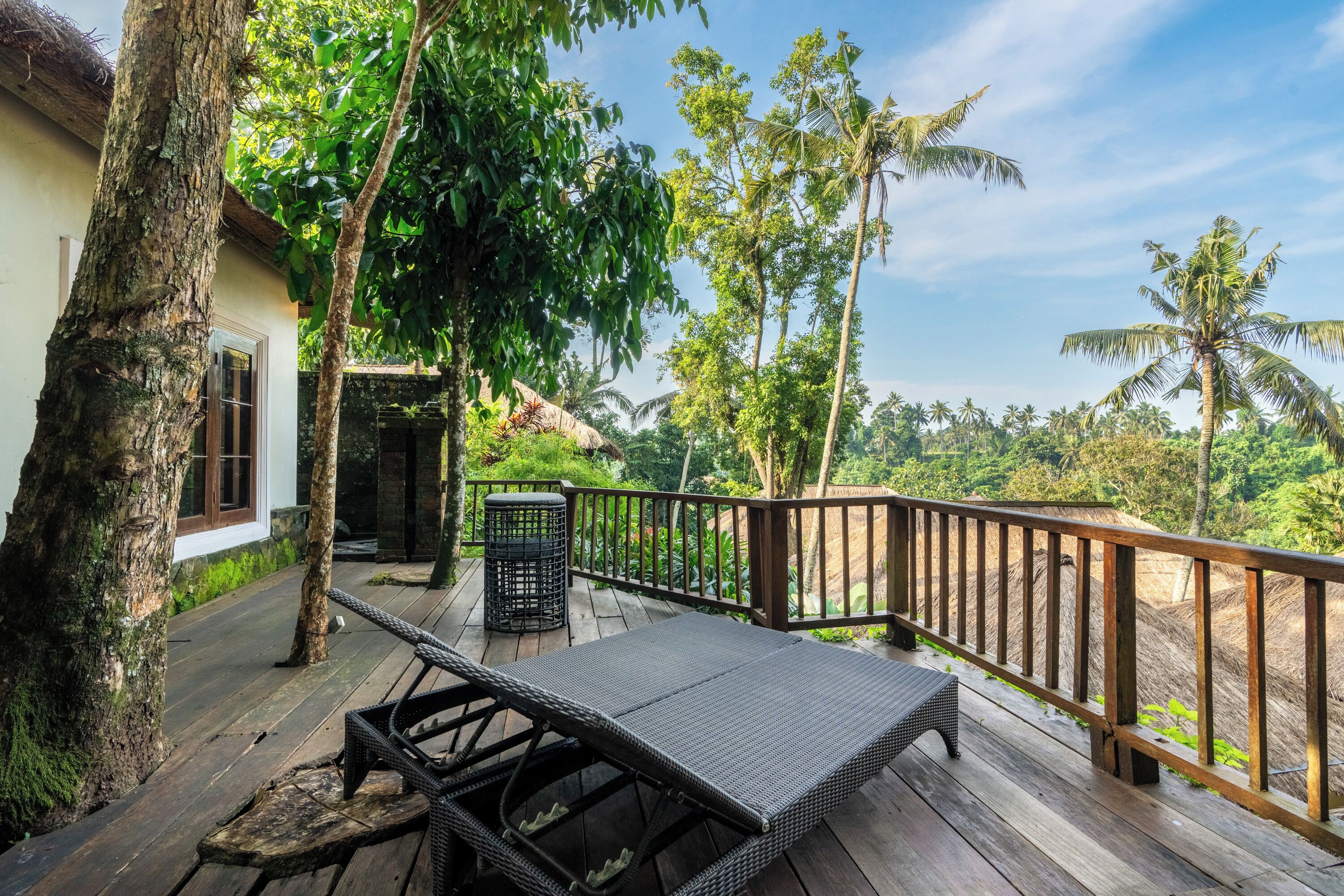A wooden deck with a table and chairs, surrounded by trees and a view of the landscape.