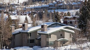 A snow-covered lodge with multiple chimneys, surrounded by trees and a ski slope in the background. - Tamarack Townhomes - CoralTree Residence Collection (Snowmass Village)