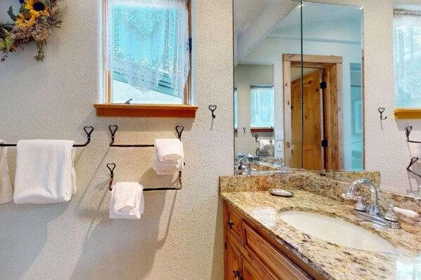 A bathroom with a granite countertop sink, wooden cabinets, and a large mirror. - Tamarack Townhomes - CoralTree Residence Collection (Snowmass Village)