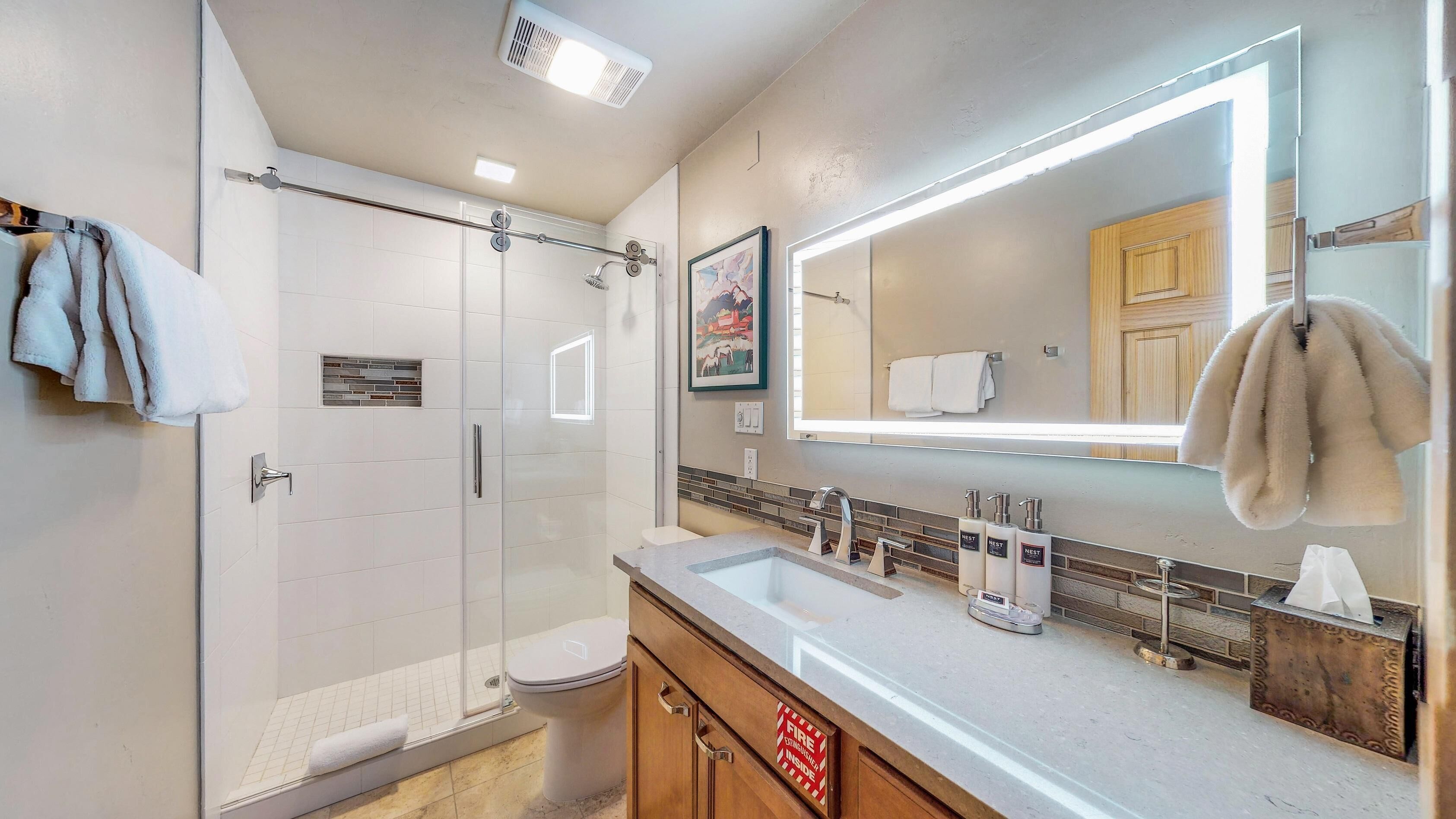 A modern bathroom with a glass shower enclosure, a toilet, a sink with a mirror, and a towel rack.