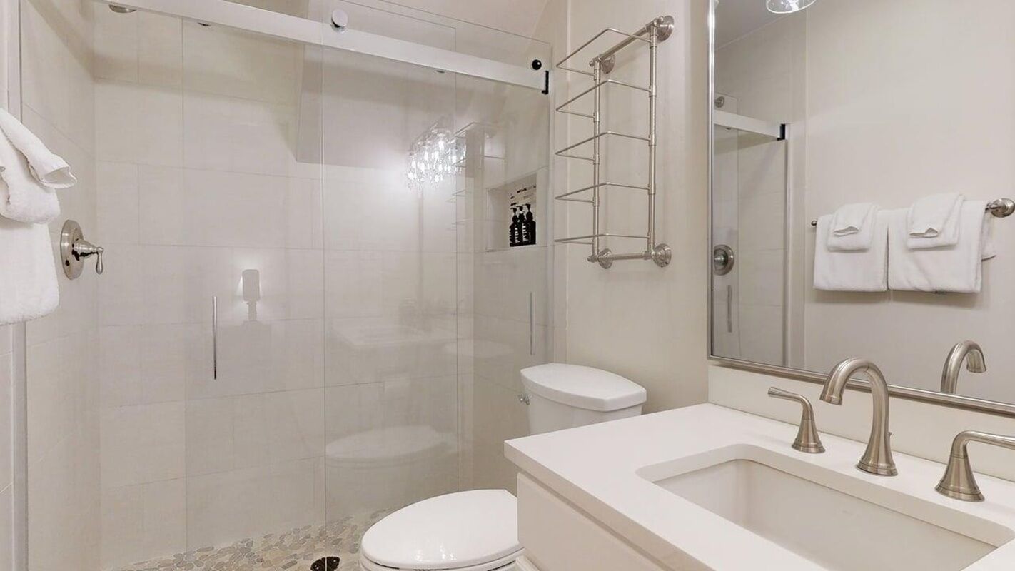 Un baño moderno con ducha envuelta en vidrio, inodoro, lavamanos con doble grifo y toallero con toallas.