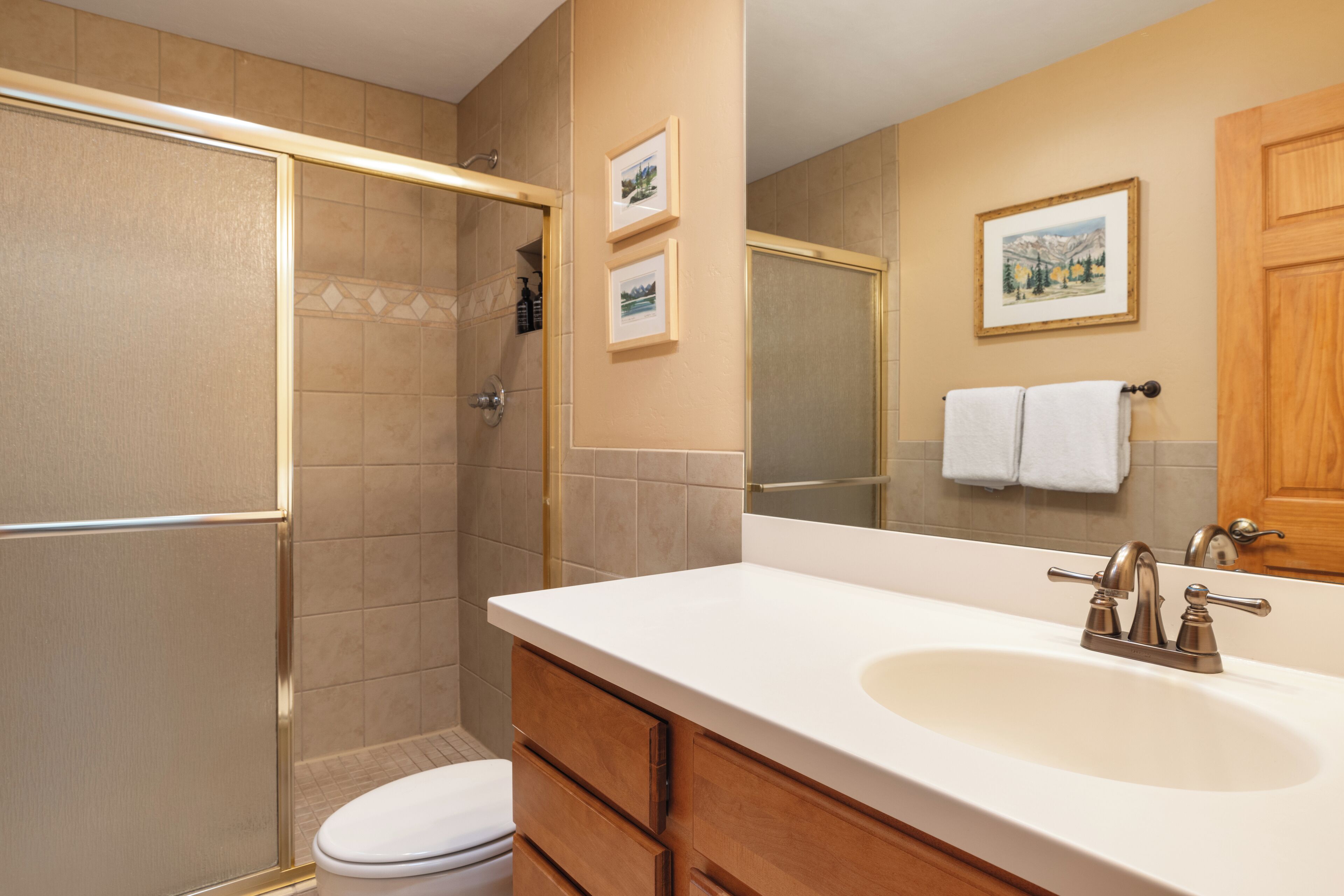 A bathroom with a shower, toilet, sink, and wooden cabinets.