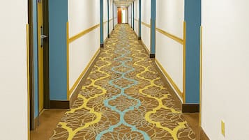 A hotel hallway with a patterned carpet, doors on both sides, and a light fixture on the ceiling.