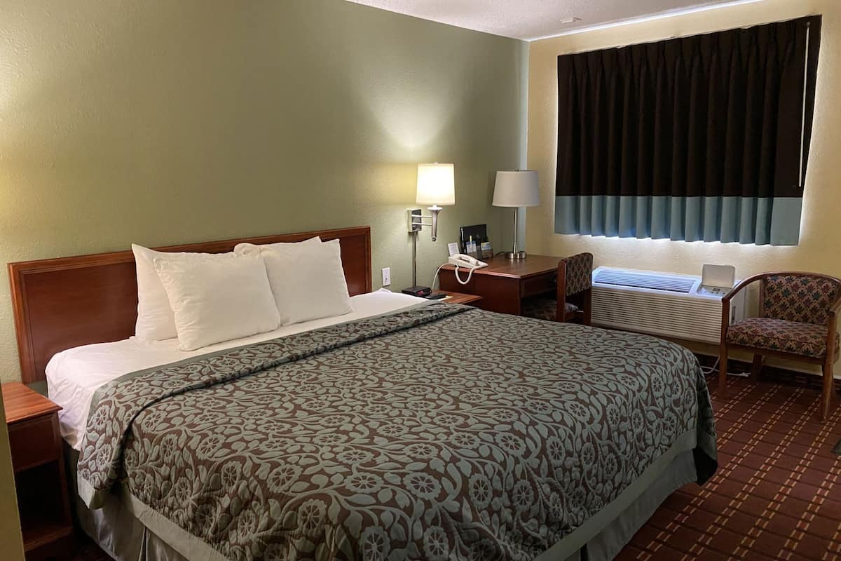 A hotel room with a large bed, a desk, a chair, a telephone, and a window with curtains.