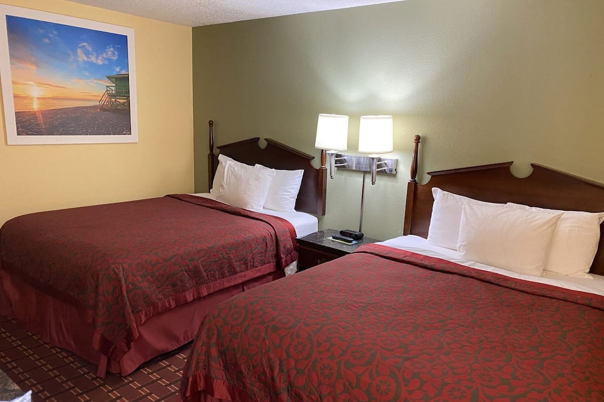 A hotel room with two beds, a nightstand, a lamp, and a painting on the wall.