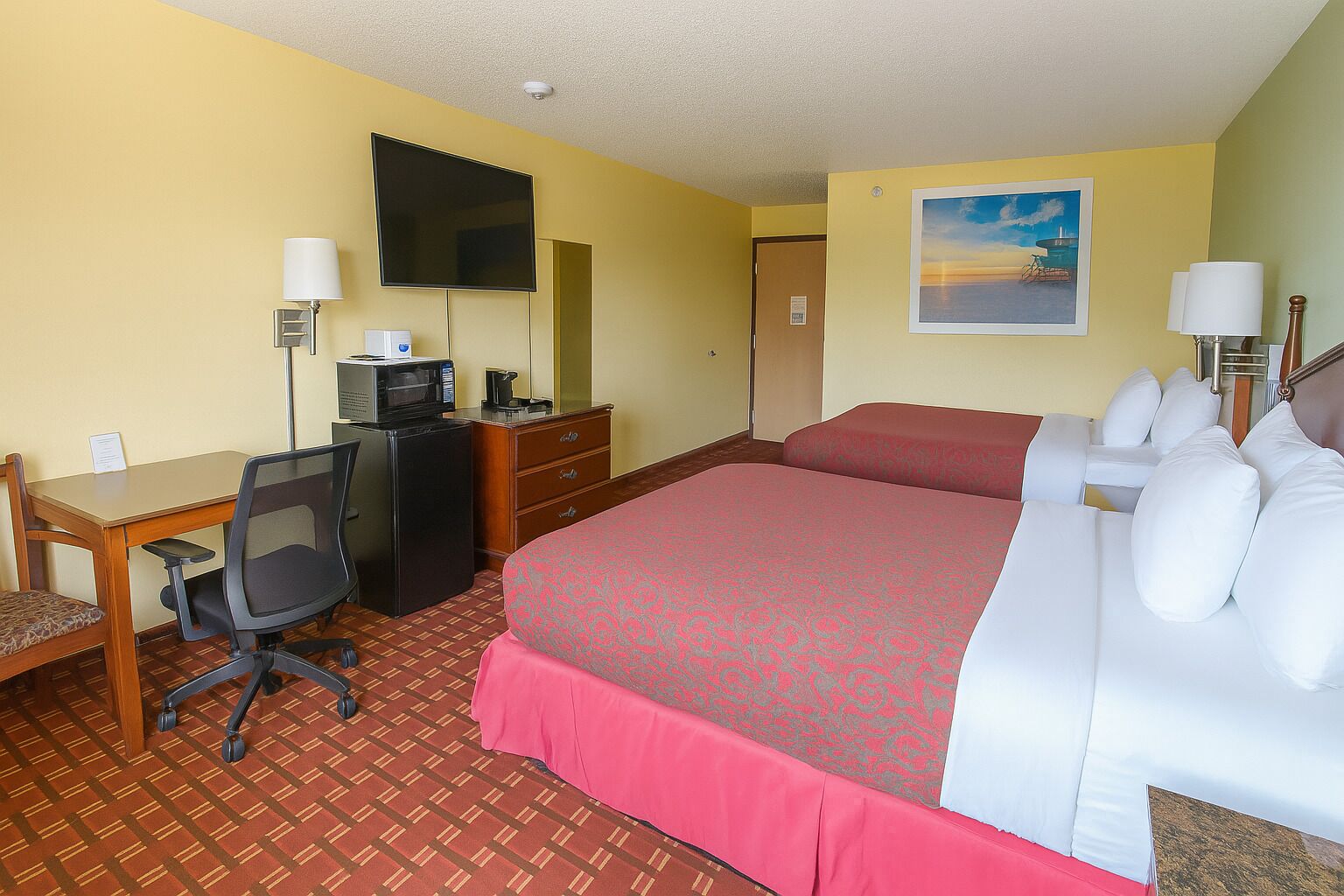 Habitación de hotel con cama, escritorio, silla, televisión y un cuadro en la pared.