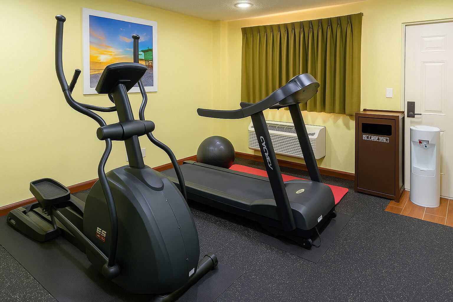 Un gimnasio con una máquina elíptica, una cinta de correr y una bicicleta estática.
