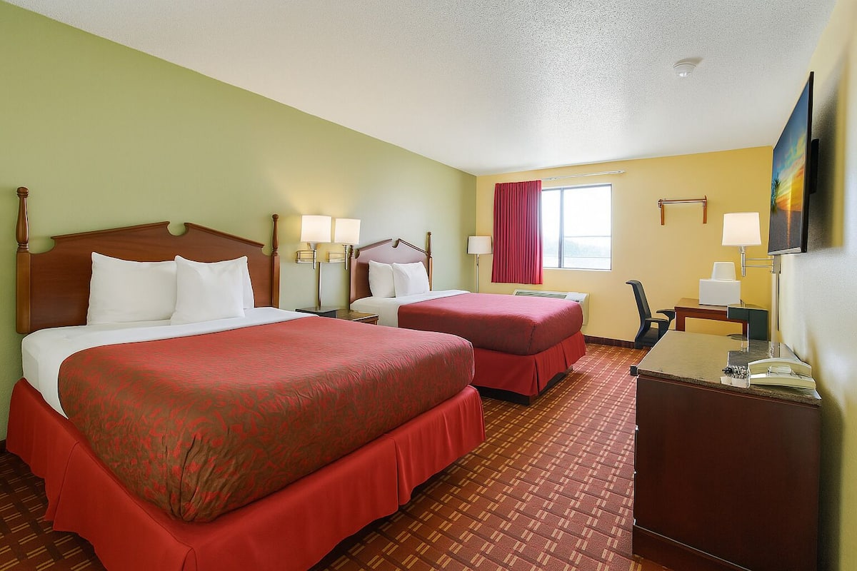 A hotel room with two beds, a desk, a chair, a TV, and a window with curtains.