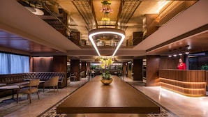 Un vestíbulo amplio con un mostrador de recepción de madera, un área de descanso cómoda con sofás y sillones, y una decoración floral central.