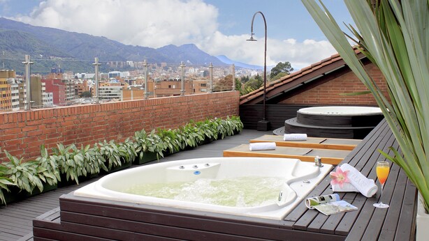 Una terraza en la azotea con hidromasaje, cubierta de madera y vistas a la ciudad y montañas.
