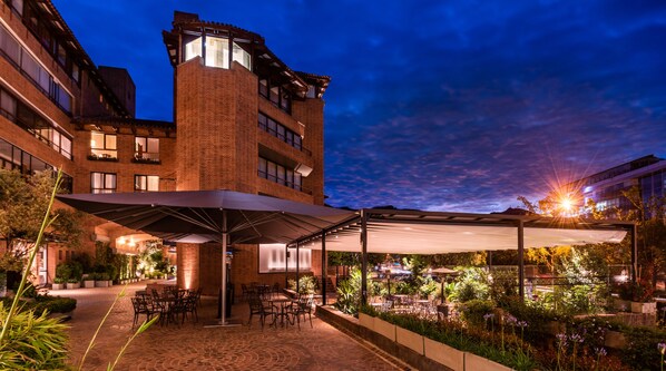 An outdoor patio area with brick flooring, outdoor seating, and a covered section with umbrellas. - Estelar Apartamentos Bogotá - La Fontana (Bogotá)
