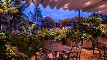 An outdoor patio with a round table and chairs, surrounded by potted plants and a metal fence.